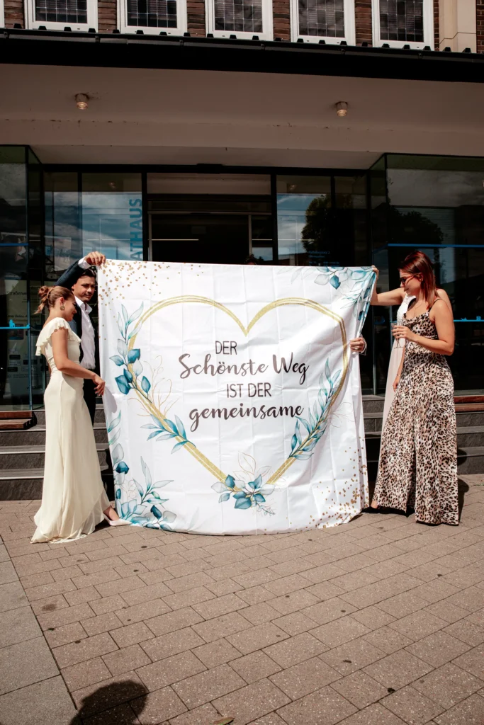 Nach der standesamtlichen Hochzeit von Steffi & Sebastian in Monheim wurde ein großes weißes Tuch in den Weg gehalten, verziert mit einem Herz und einem liebevollen Spruch.